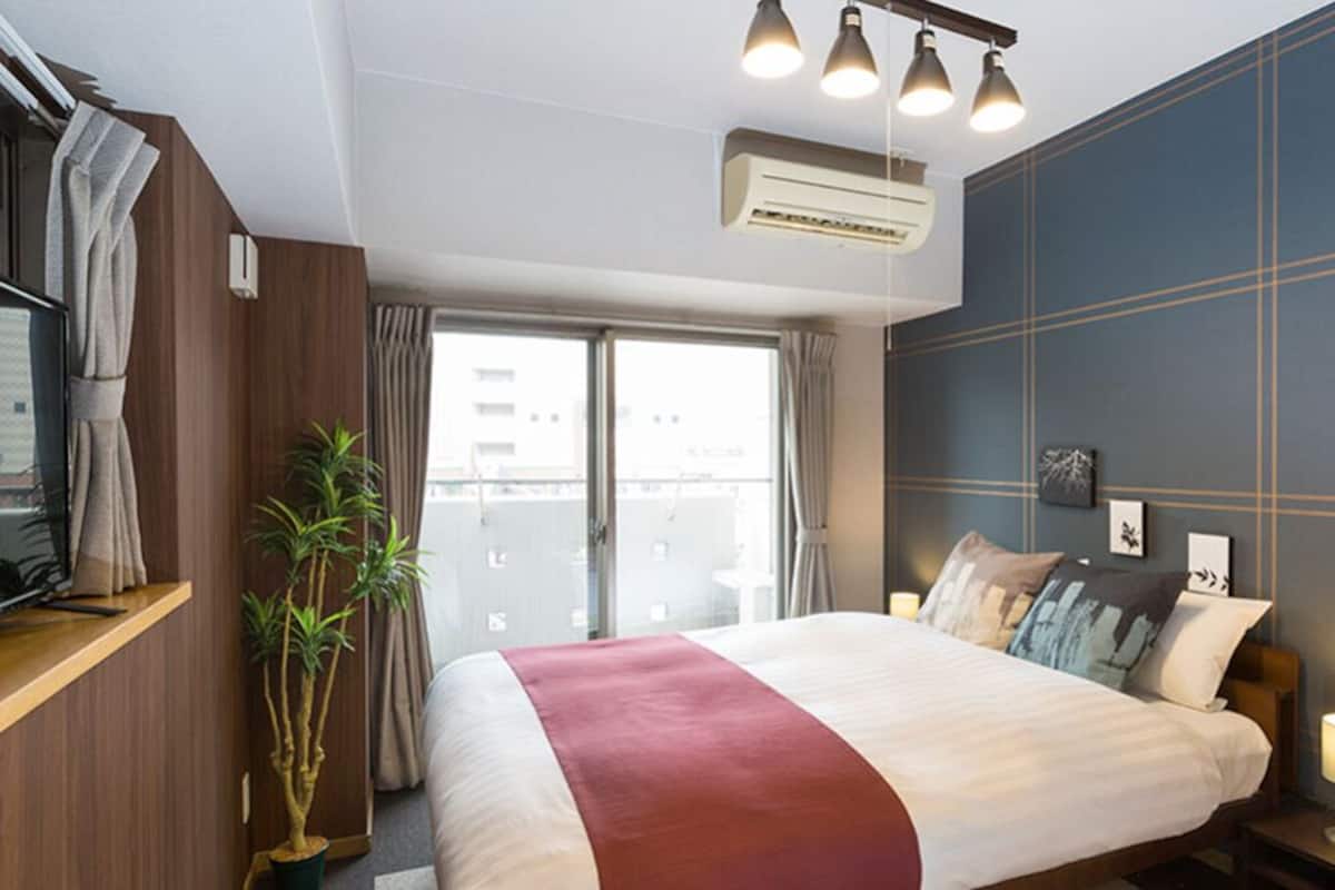 A hotel room with a bed, a TV, a plant, and a window with curtains.