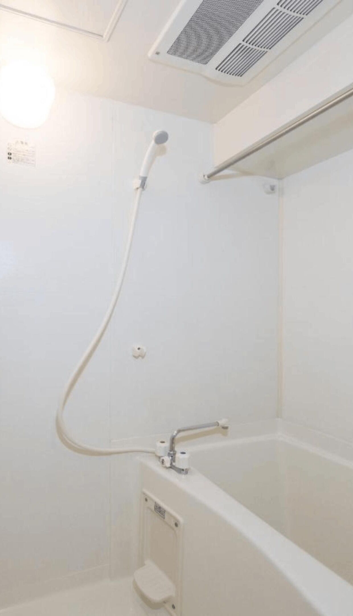 A small, white, enclosed shower area with a handheld showerhead and a built-in bathtub.