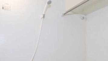 A small, white, enclosed shower area with a handheld showerhead and a built-in bathtub.