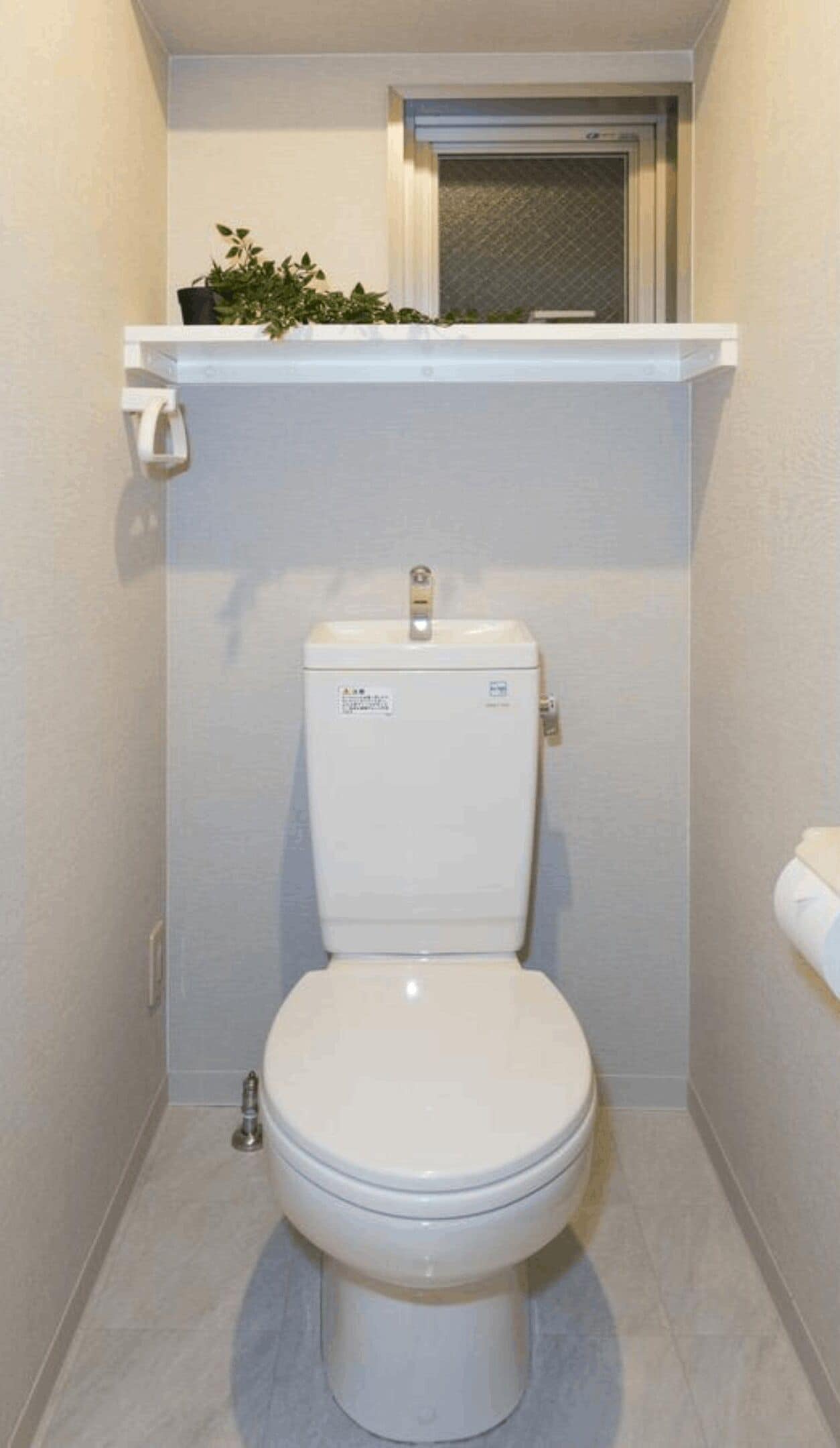 Un baño pequeño con inodoro blanco, un estante sobre el inodoro y una puerta que da a otra habitación.