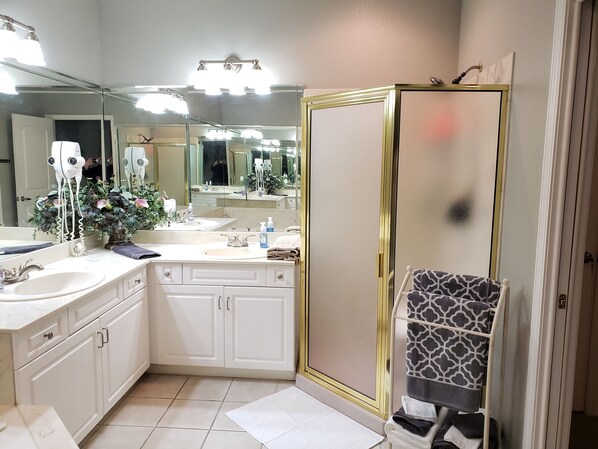 A bathroom with two sinks, a large mirror, a shower with a gold frame, and a towel rack.