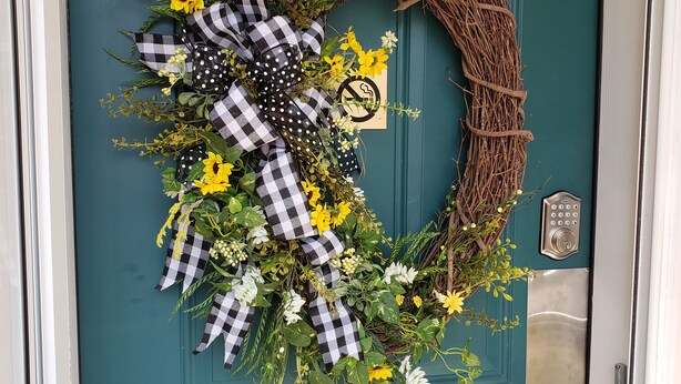 Una puerta azul verdoso con un adorno de flores, hojas y un lazo de cuadros.