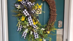 A teal door with a wreath made of flowers, leaves, and a checkered ribbon.