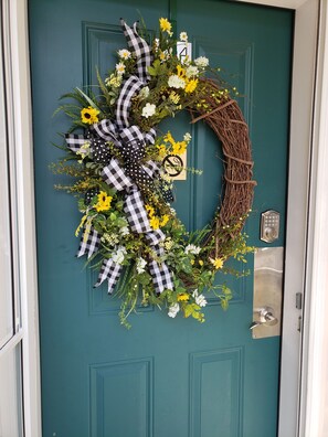 A teal door with a wreath made of flowers, leaves, and a checkered ribbon.