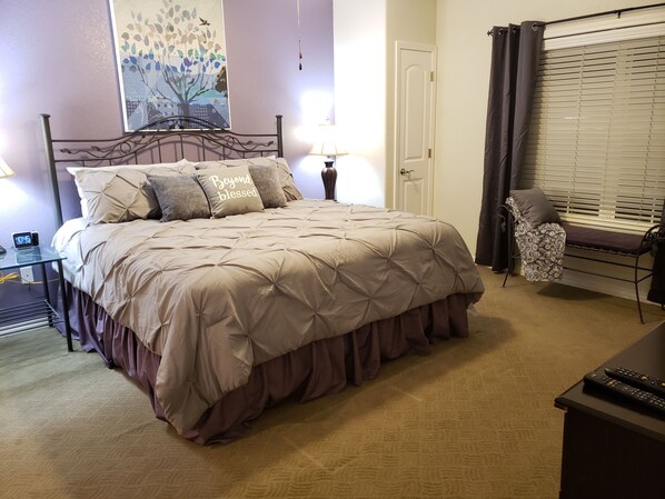 Un dormitorio ordenado con cama, lámparas de noche, una silla y una puerta.