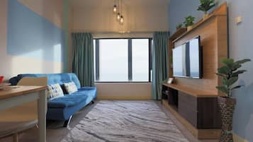 A modern living room with a blue sofa, a wooden TV stand, a large window with curtains, and a patterned rug.