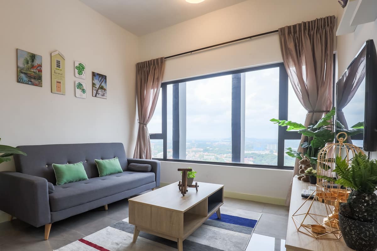 Een moderne woonkamer met een grijze bank, een houten salontafel en een groot raam met gordijnen.
