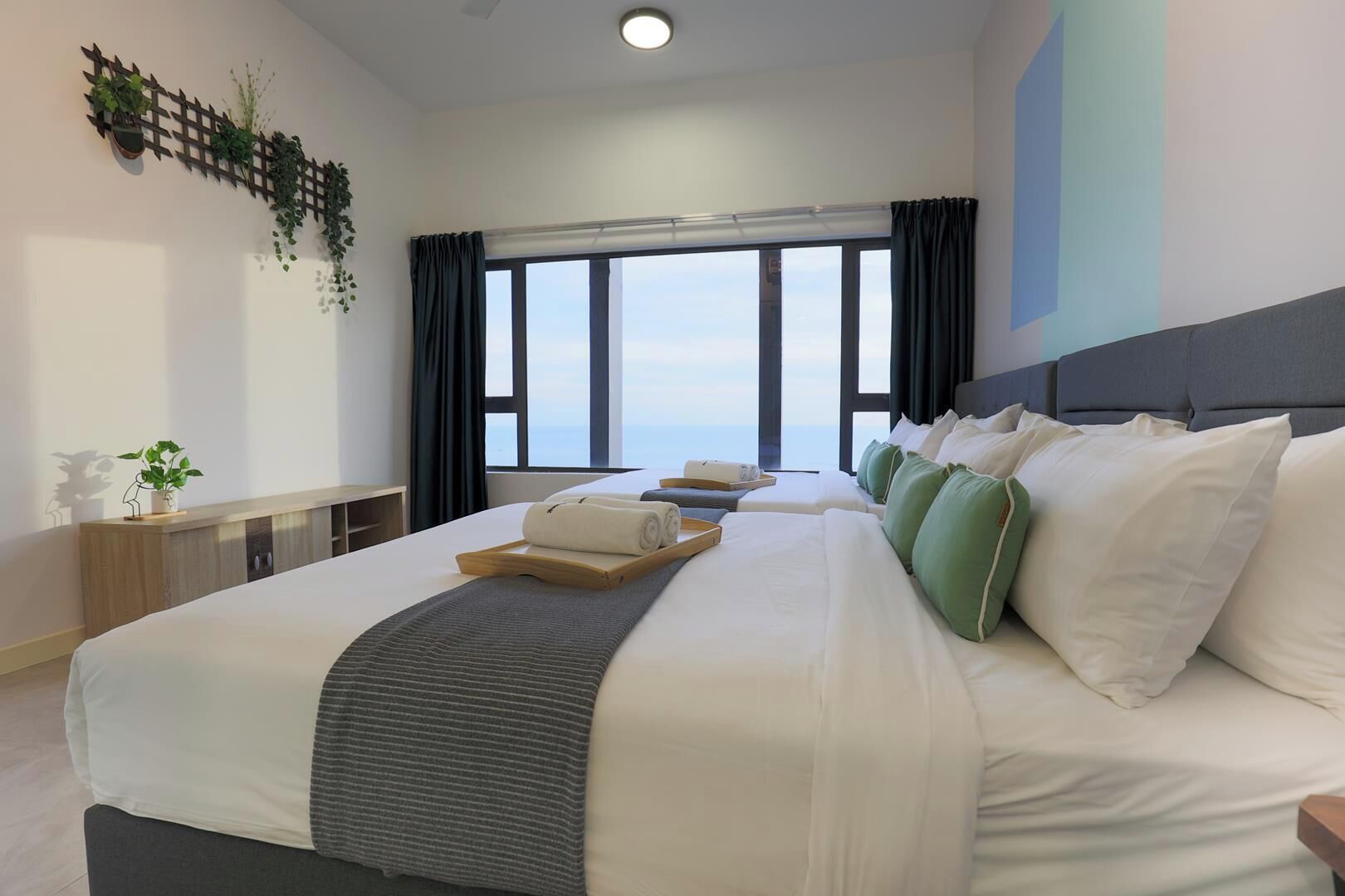 A hotel room with a large bed, a view of the sea, and a wooden console table with a plant.