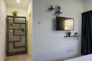 Un salon moderne avec un téléviseur fixé au mur, une porte à motifs géométriques et des plantes en pot disposées sur des étagères.