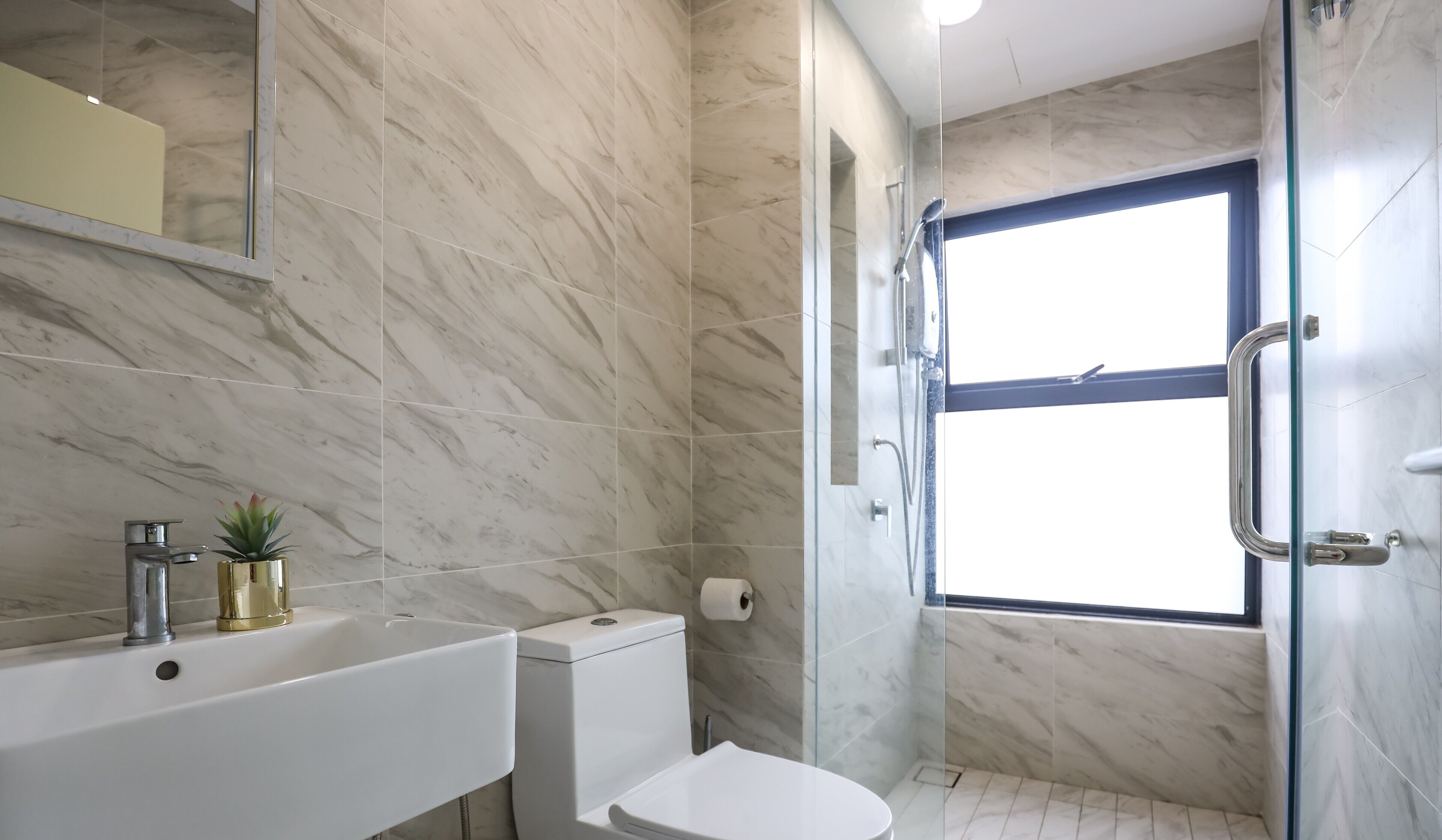 Une salle de bain avec un sol en marbre, un lavabo blanc, des toilettes et une douche séparée par une paroi en verre.