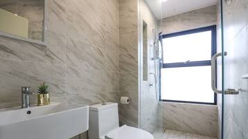 Une salle de bain avec un sol en marbre, un lavabo blanc, des toilettes et une douche séparée par une paroi en verre.
