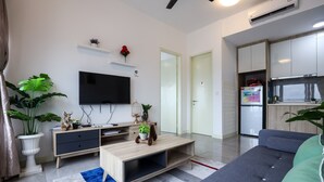 A modern living room with a flat-screen TV, a wooden coffee table, and a sofa. There is a kitchen area with a refrigerator and a microwave. - Imperio Seaview Melaka By I Housing (Malacca City)