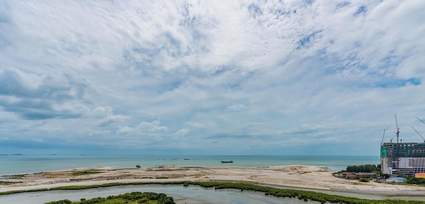 Un paysage côtier comprenant une plage, une étendue d’eau et un chantier de construction avec des grues.