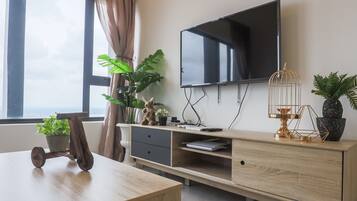 A modern living room with a flat-screen TV mounted on the wall, a wooden coffee table, a desk with a laptop, and various decorative items including plants and a birdcage.