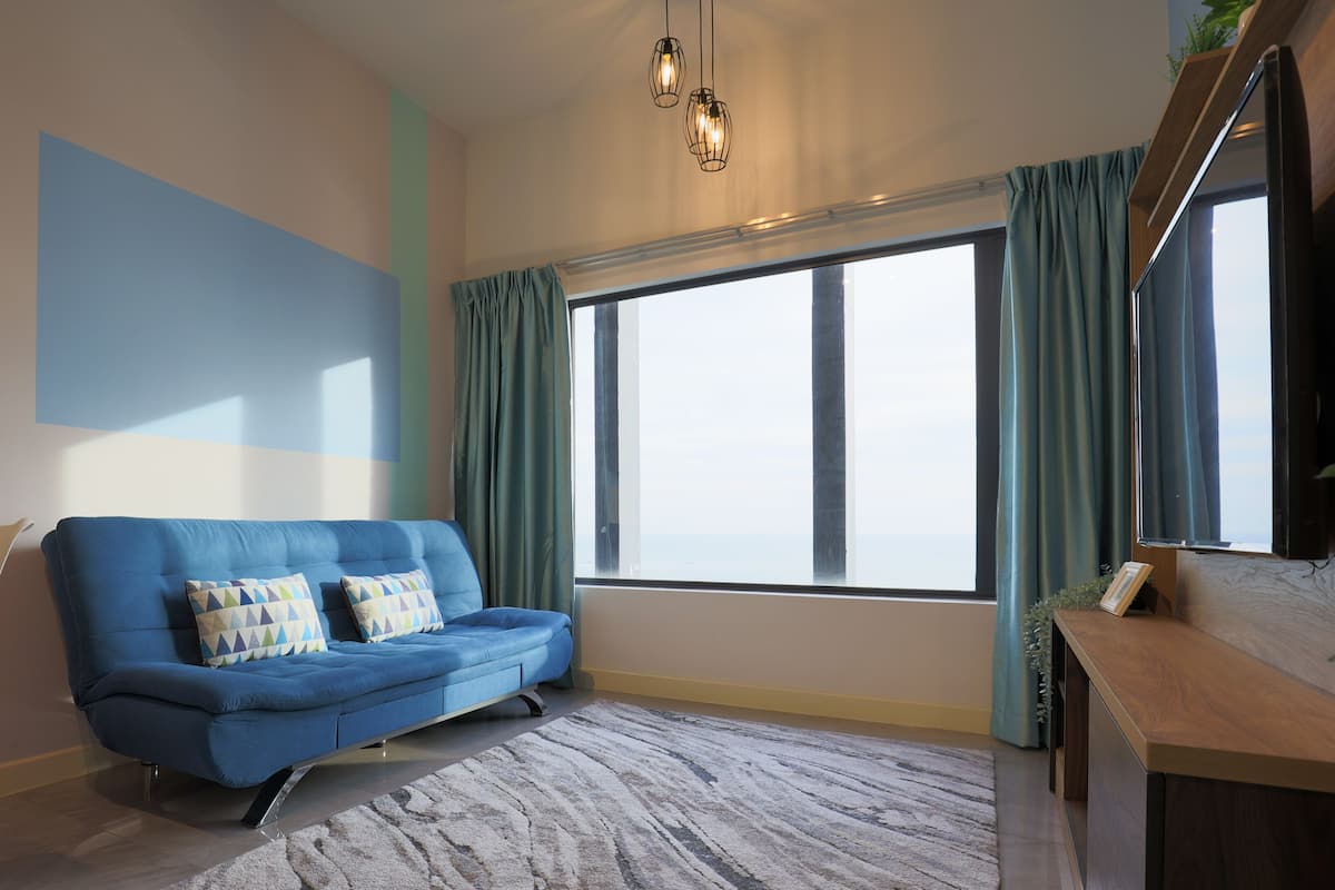 Een moderne woonkamer met een blauwe bank, een houten salontafel en een groot raam met gordijnen.
