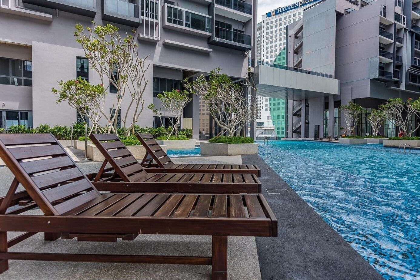 Un hotel moderno con piscina, sdraio e vista sugli edifici circostanti.