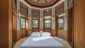 A bedroom with a large bed, wooden walls, and windows with blinds.