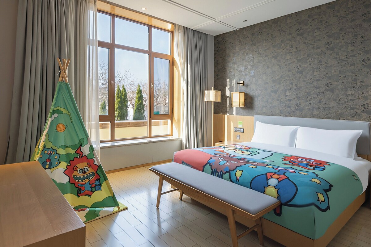 A hotel room with a large bed, a bench, a window with curtains, and a wall with a textured pattern.