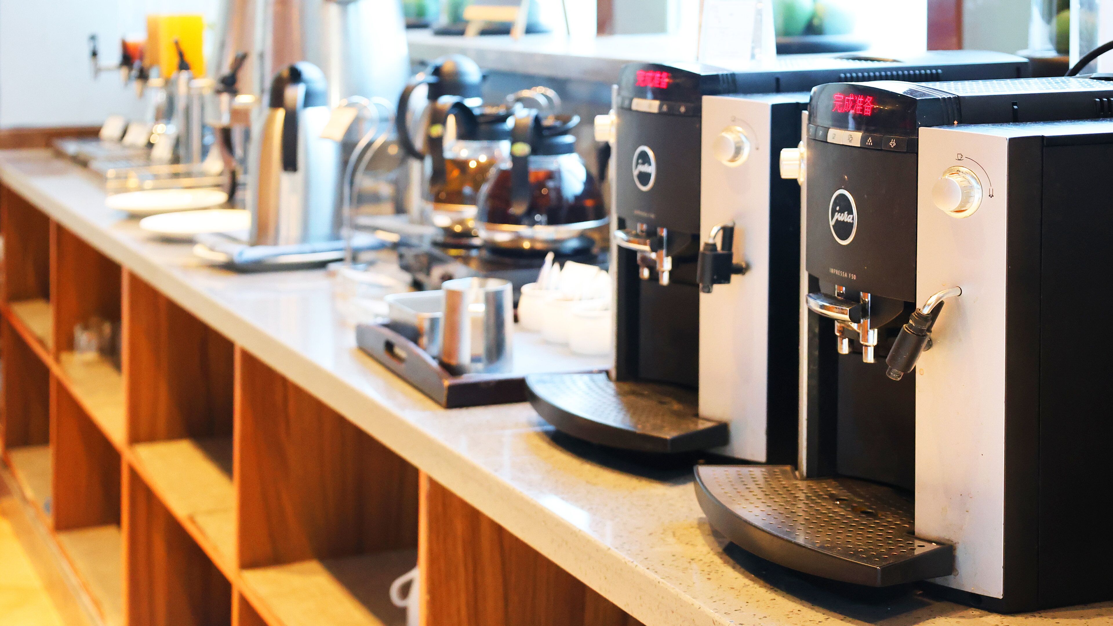 Varias máquinas de espresso en una barra con un estante de madera al fondo.
