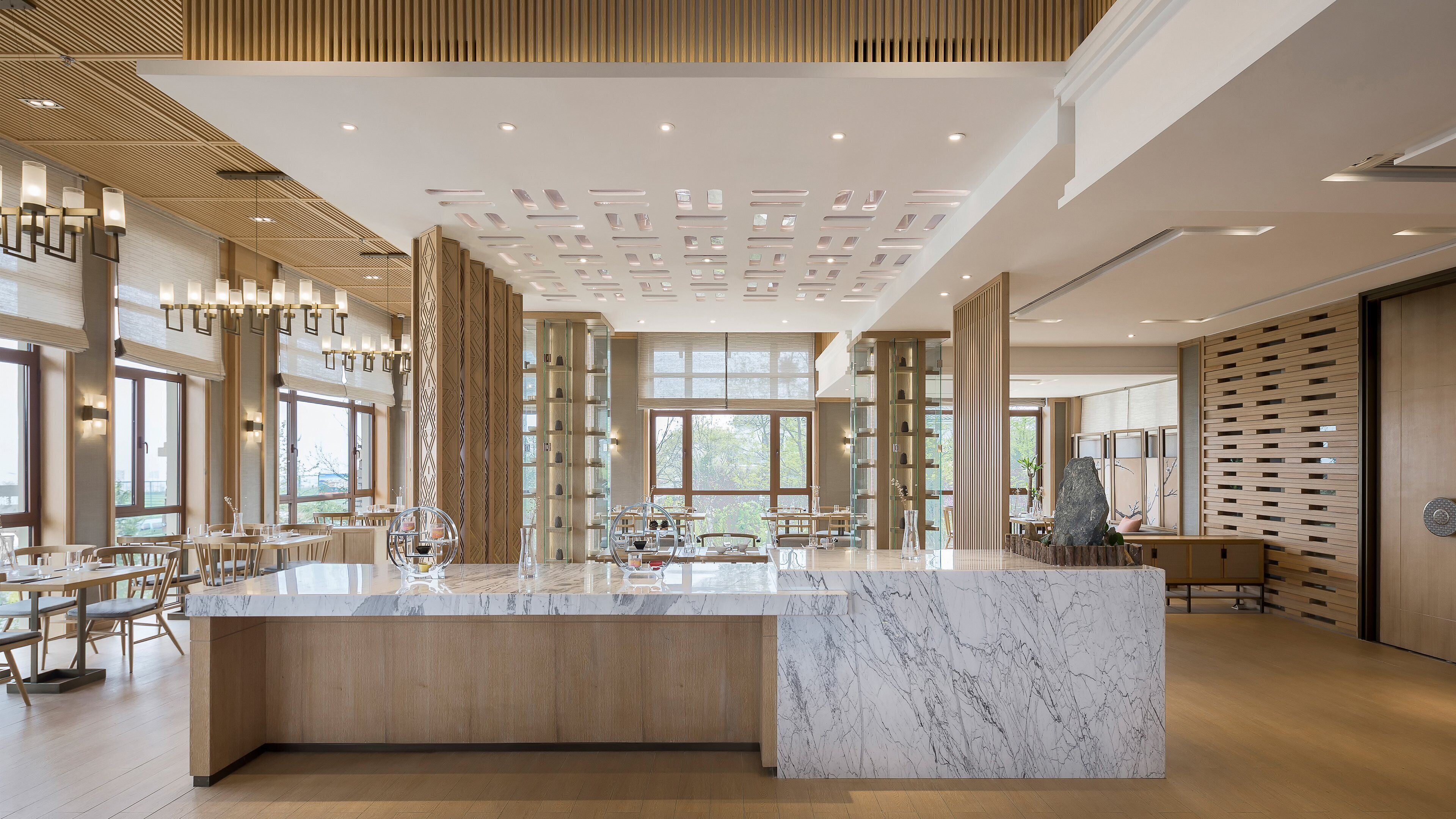 Un moderno vestíbulo de hotel con una recepción de mármol, paneles de madera y amplias ventanas.