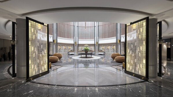 A spacious lobby with a central seating area, a polished marble floor, and a large window providing natural light.
