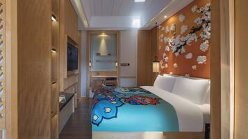 A hotel room with a bed, a desk, a chair, a TV, and a wall with a floral design.