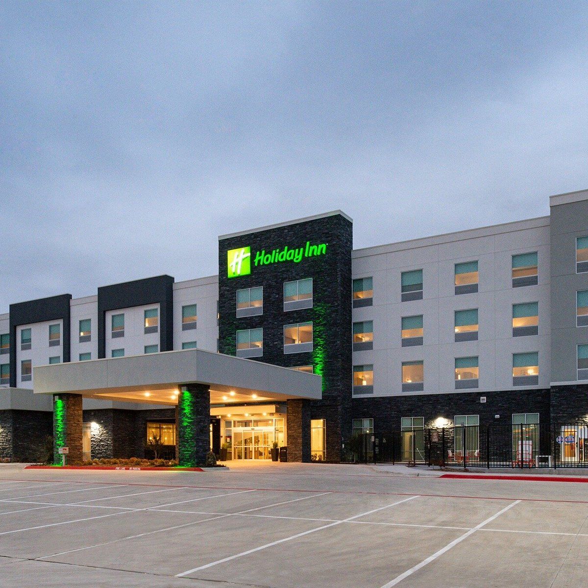 A Holiday Inn hotel with a modern facade, a large parking lot, and a well-lit entrance.