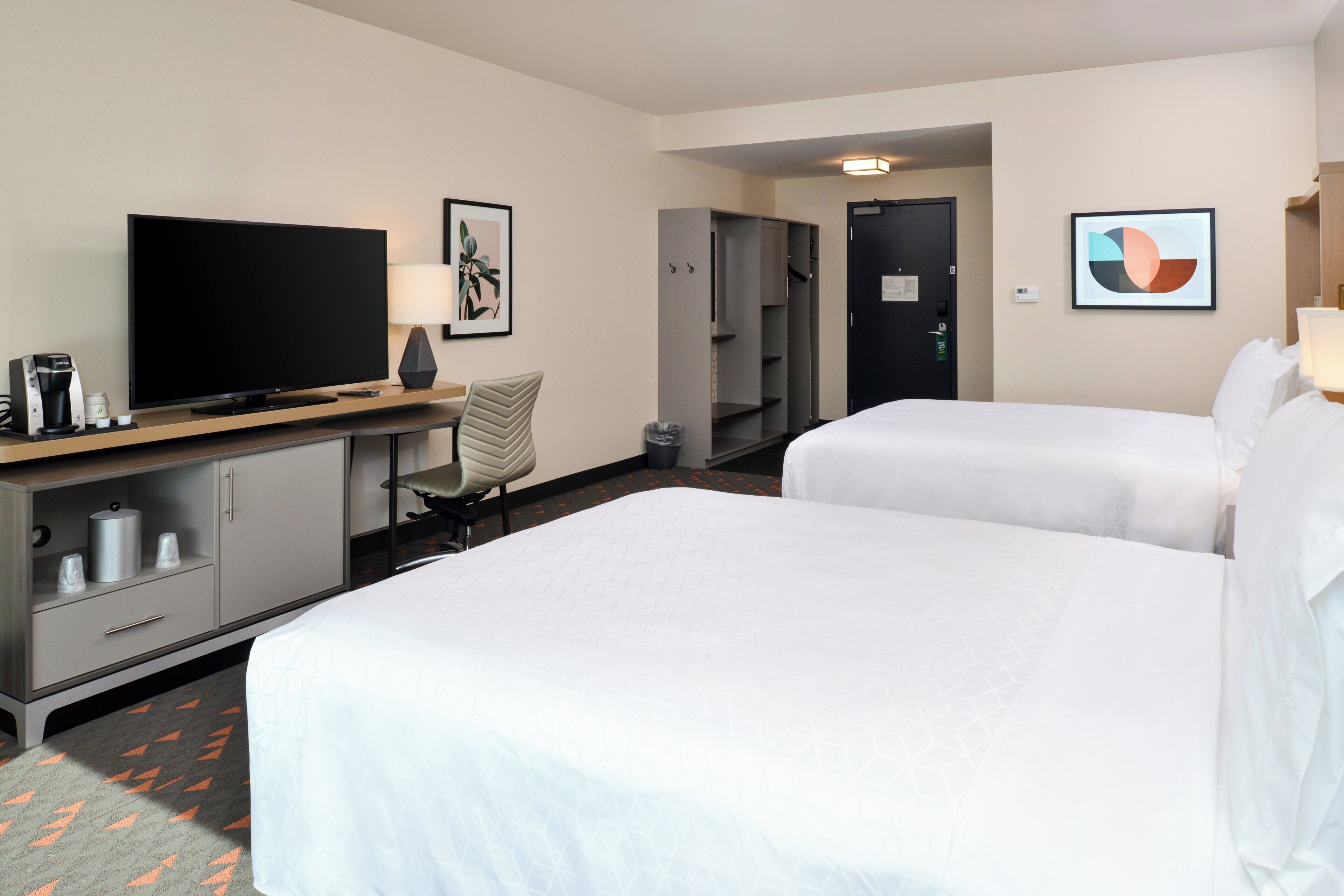 Habitación de hotel con dos camas, un televisor, un escritorio con lámpara, una silla y un armario.