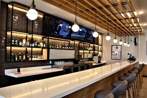 A bar area with a long counter, multiple bar stools, hanging pendant lights, and shelves stocked with bottles and glasses. - Holiday Inn Fort Worth - Alliance by IHG (Keller)