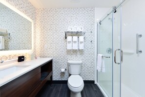 A modern bathroom with a toilet, a glass shower enclosure, a sink with a mirror, and a patterned wall. - Holiday Inn Fort Worth - Alliance by IHG (Keller)