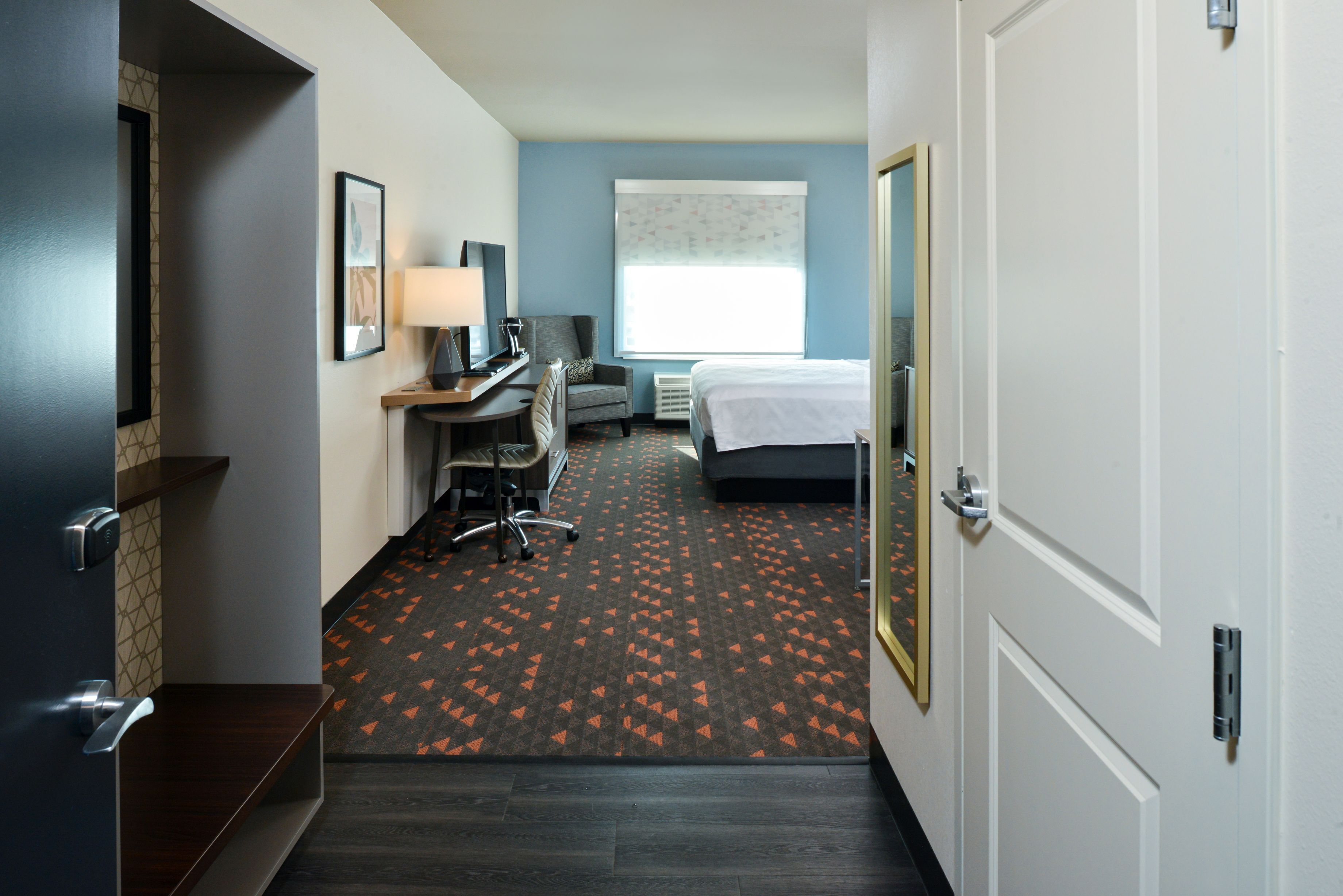 A hotel room with a bed, desk, chair, and a window with a view.