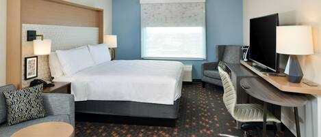 A hotel room with a bed, a desk with a TV, a chair, a small table, and a sofa.