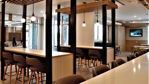 Zona de bar moderna con taburetes altos, iluminación colgante y un televisor de pantalla plana mostrando un evento deportivo.