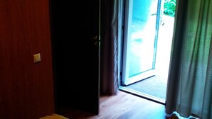 A room with a bed, a door leading to a balcony, and a view of greenery outside. - ATRIUM Guesthouse (Riga)