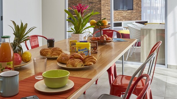 A modern dining area with a wooden table, red chairs, and a ceiling light fixture. - Nemea Beaux arts (Montpellier)