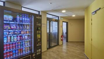 A vending machine with snacks and drinks, a fire extinguisher, and a glass door leading to another room.
