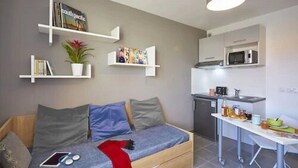A compact living space with a sofa, a small kitchen area, and built-in shelves. - Nemea Beaux arts (Montpellier)