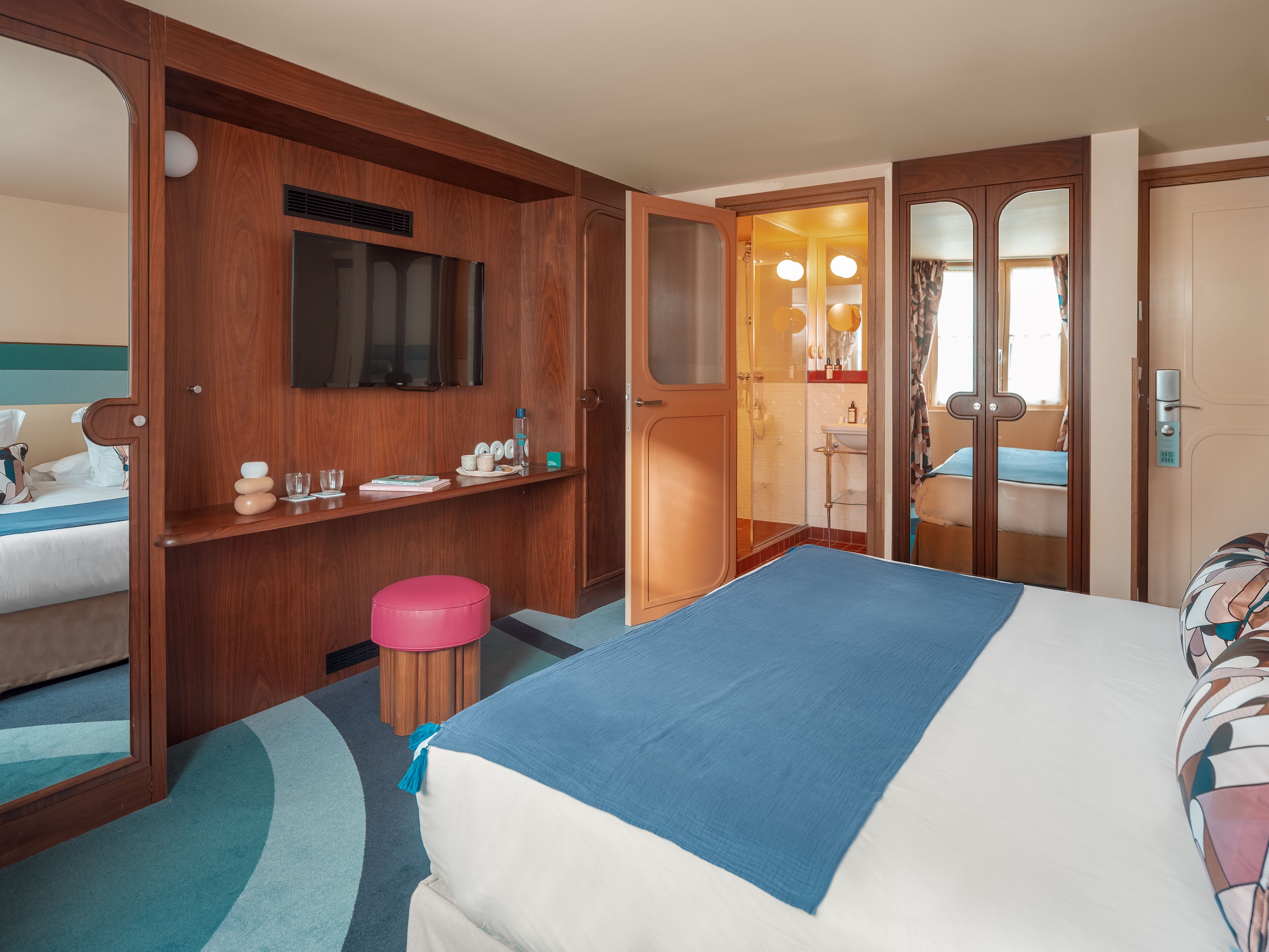 Een hotelkamer met een bed, een bureau, een spiegel en een badkamer zichtbaar door een geopende deur.