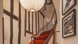 Een spiraaltrap met tredes bekleed met rood tapijt, een houten leuning en een witte hanglamp.