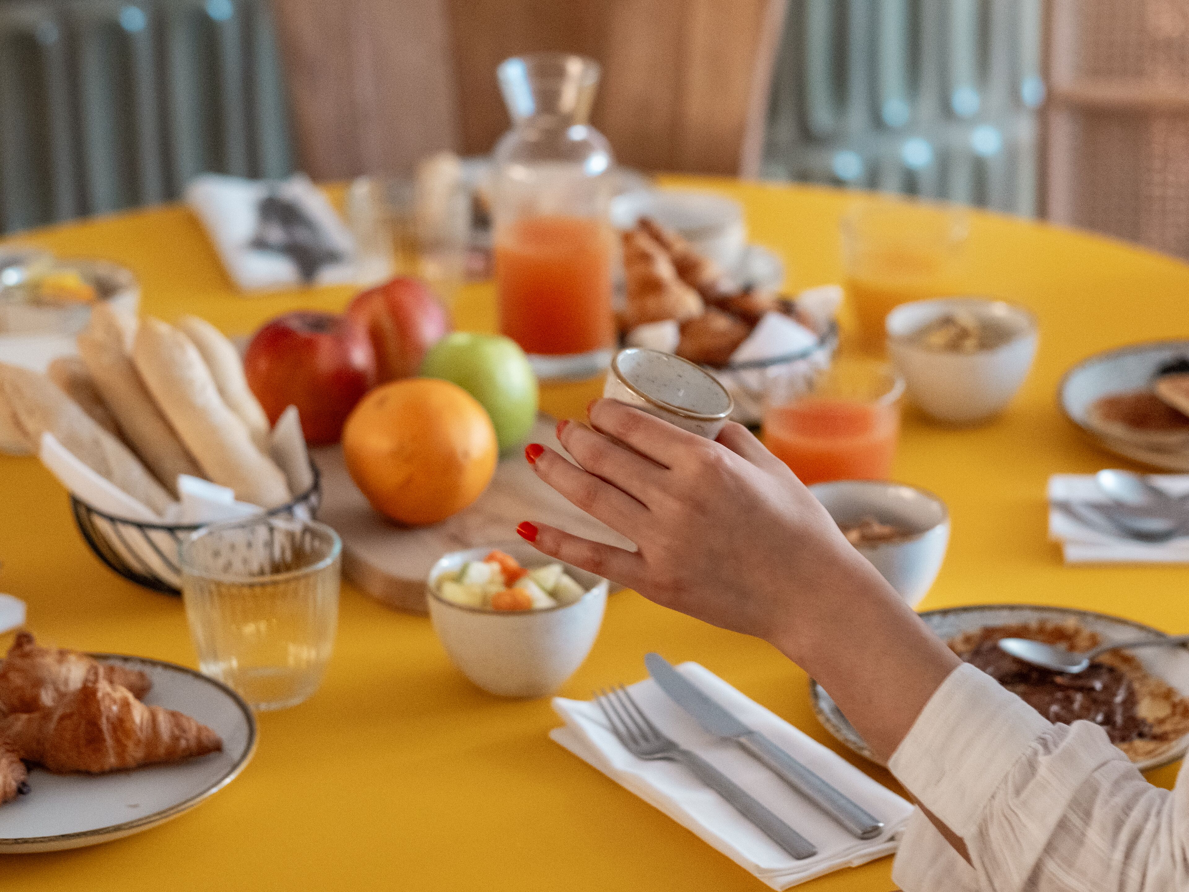 Una mesa de desayuno con cruasanes, frutas, un vaso de zumo de naranja y una taza de café.