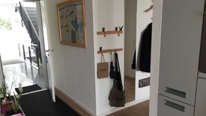 A hallway with a staircase, a wall-mounted coat rack, a door with a handle, and a potted plant. - Boardinghouse Oelde - Apartment mit Terrasse (Oelde)