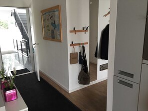Een gang met een trap, een kapstok aan de muur, een deur met een handgreep en een potplant.