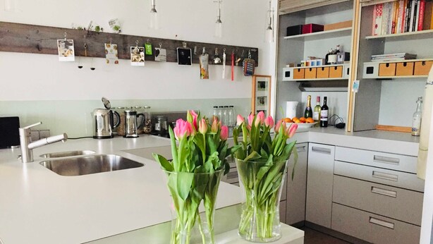 A modern kitchen with a central island, stainless steel appliances, and a wooden backsplash. - Boardinghouse Oelde - Apartment mit Terrasse (Oelde)