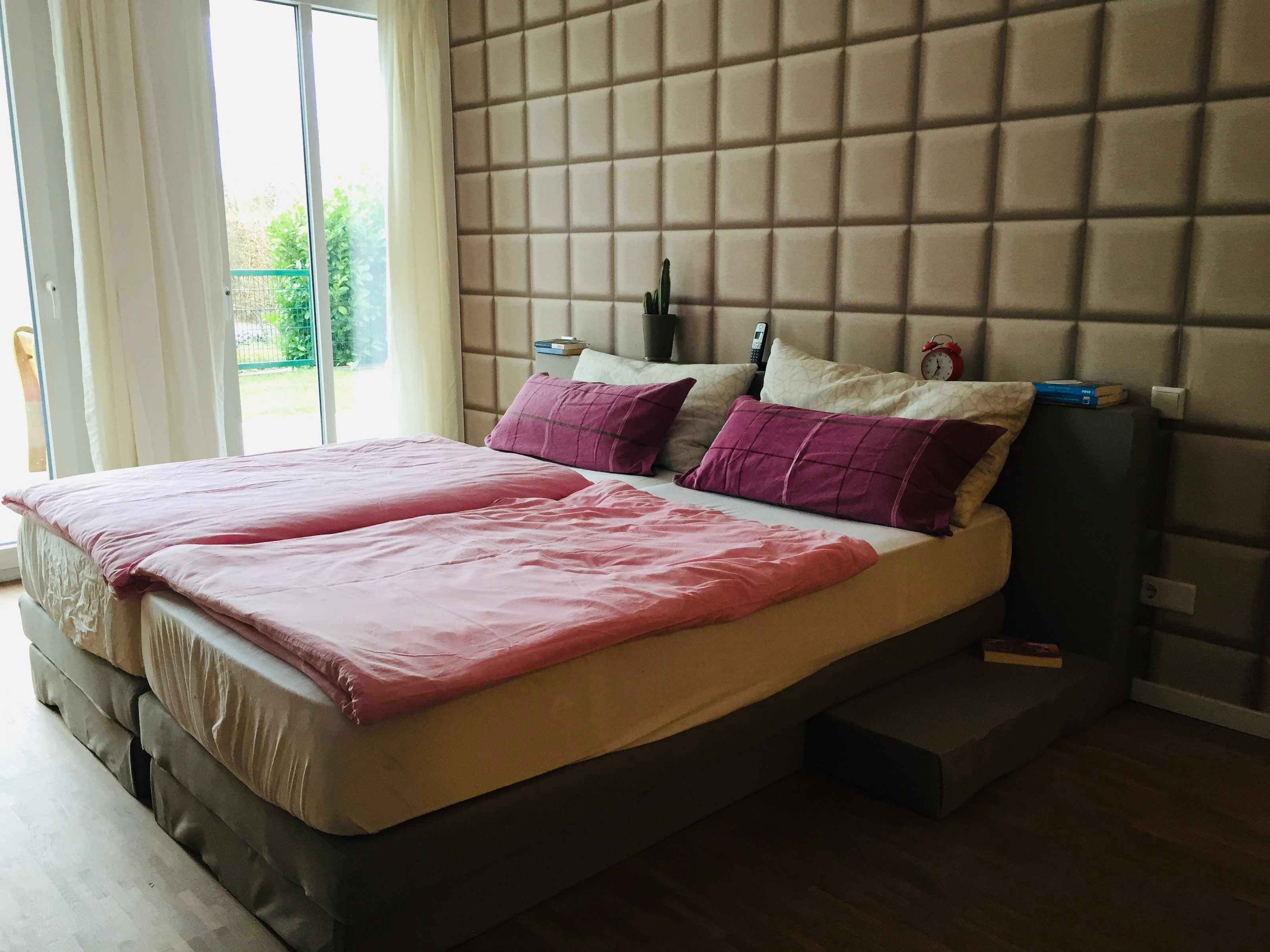 Ein Schlafzimmer mit einem Bett, Kissen, einem Nachttisch und einem Fenster.
