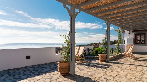 A rooftop terrace with a view of the sea, potted plants, and a wooden chair.