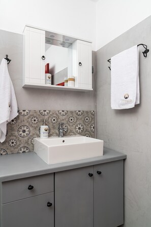 A bathroom with a white sink, a mirror above it, and patterned tiles on the wall. - Kalliope Studios (Karpathos)
