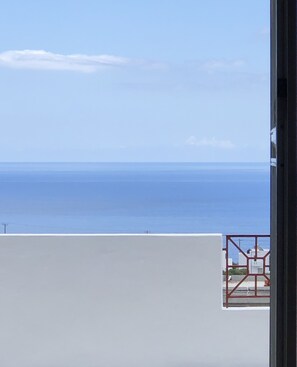 A view of the sea from a balcony with a white wall in the foreground and a red railing. - Kalliope Studios (Karpathos)