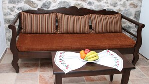 A wooden sofa with striped cushions against a stone wall, a table with a placemat and fruit. - Cavo Ponta (Gortyna)