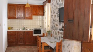 A kitchen with wooden cabinets, a tiled backsplash, a dining table with chairs, a microwave, and a television mounted on the wall. - Cavo Ponta (Gortyna)