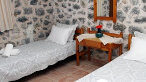 A room with two single beds, a wooden table with a vase of flowers, and a stone wall. - Cavo Ponta (Gortyna)